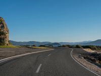 a empty road leading towards mountains in the distance with trees on one side and blue skies in the other