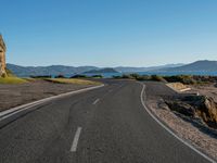 a empty road leading towards mountains in the distance with trees on one side and blue skies in the other