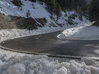 a motorcycle traveling on a snowy road by a wall in the woods of some mountains