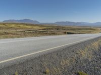 a motorcycle traveling on an empty rural highway with mountain in the background and no people in the area