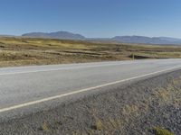 a motorcycle traveling on an empty rural highway with mountain in the background and no people in the area