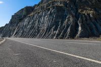 the man is riding his bike down the paved street beside rocks and boulders in the mountains