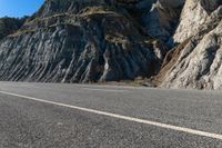 the man is riding his bike down the paved street beside rocks and boulders in the mountains