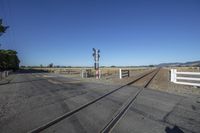 an empty train track runs along the side of a mountain in the distance, a white picketer and a white fence