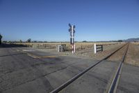 an empty train track runs along the side of a mountain in the distance, a white picketer and a white fence