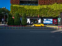 a yellow car and some green bushes in the street below it is a building with a green roof on top