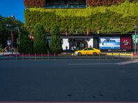 a yellow car and some green bushes in the street below it is a building with a green roof on top