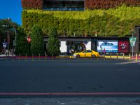 a yellow car and some green bushes in the street below it is a building with a green roof on top