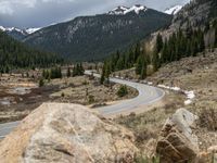 a mountain side with a road running next to the mountains, a bike parked in front of it and trees on one side