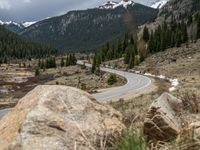 a mountain side with a road running next to the mountains, a bike parked in front of it and trees on one side