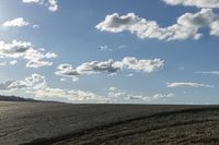 a lone jet flies over a large empty field of dry grass on a cloudy day