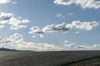 a lone jet flies over a large empty field of dry grass on a cloudy day