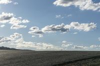 a lone jet flies over a large empty field of dry grass on a cloudy day