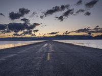 a lone asphalt road running along the shore at dusk by the sea or lake with beautiful clouds