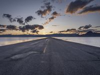 a lone asphalt road running along the shore at dusk by the sea or lake with beautiful clouds