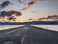 a lone asphalt road running along the shore at dusk by the sea or lake with beautiful clouds