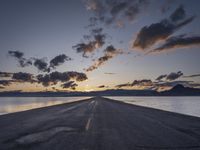 a lone asphalt road running along the shore at dusk by the sea or lake with beautiful clouds