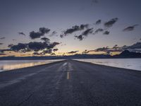 a lone asphalt road running along the shore at dusk by the sea or lake with beautiful clouds