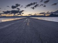 a lone asphalt road running along the shore at dusk by the sea or lake with beautiful clouds