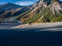 a black car driving down the highway near mountains in the fall time at dusk with a clear blue sky