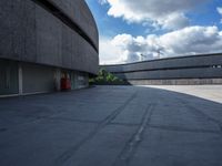 a concrete building has a red fire hydrant in a courtyard area with clouds overhead