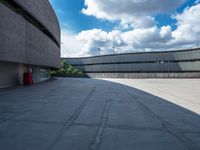 a concrete building has a red fire hydrant in a courtyard area with clouds overhead