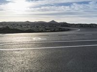 an empty road lined with circular lanes under a blue sky with clouds above it and on a rocky hillside top