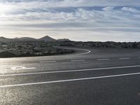 an empty road lined with circular lanes under a blue sky with clouds above it and on a rocky hillside top