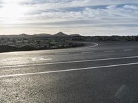 an empty road lined with circular lanes under a blue sky with clouds above it and on a rocky hillside top