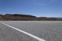 a yellow van is driving down the empty road at an angle by a mountain, the road is dotted with white lines