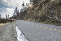 the view of a curve on a long road through some trees and rocks near the edge