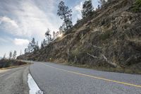 the view of a curve on a long road through some trees and rocks near the edge