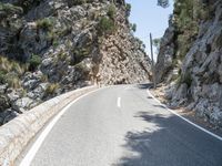 the curve of an asphalted road is lined with rocks and trees below it, along with a light blue sky and a clear sky