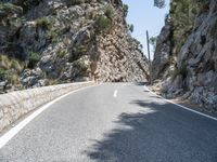 the curve of an asphalted road is lined with rocks and trees below it, along with a light blue sky and a clear sky