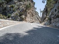 the curve of an asphalted road is lined with rocks and trees below it, along with a light blue sky and a clear sky