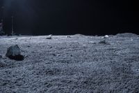 an astronaut walking in the dark on a moon area with rocks and other debris lying around