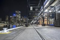 a bench next to some tracks in front of a river and a city at night