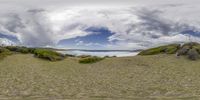 a picture of the beach near a grassy shore under a cloudy sky that looks like a panorama