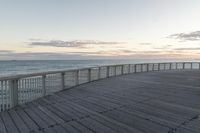 a person sits on a bench next to the ocean in the morning, and looks over the boardwalk