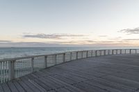 a person sits on a bench next to the ocean in the morning, and looks over the boardwalk