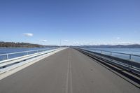 an empty bridge with a long view in the background of water, mountains and a bright sky