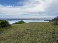 a grassy field with some water and the ocean in the background at a rocky shore