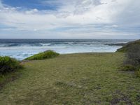 a grassy field with some water and the ocean in the background at a rocky shore