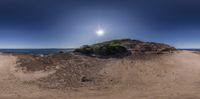 a lone beach at the edge of the water and rocks, in front of the sun