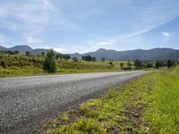 an empty rural roadway on a sunny day with mountain background and grass growing along a path