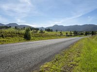 an empty rural roadway on a sunny day with mountain background and grass growing along a path