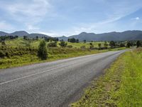 an empty rural roadway on a sunny day with mountain background and grass growing along a path