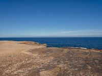 the blue ocean is very close to the shoreline and rocks, while a boat sits in the background