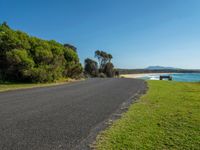 a bench sits on the edge of the empty road by the water's edge