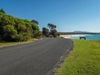 a bench sits on the edge of the empty road by the water's edge